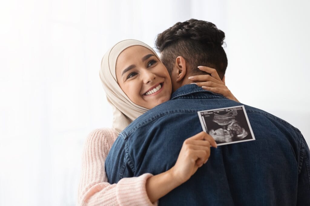 Expecting Baby. Cheerful Pregnant Muslim Woman Hijab Holding Ultrasound Picture, Hugging Husband