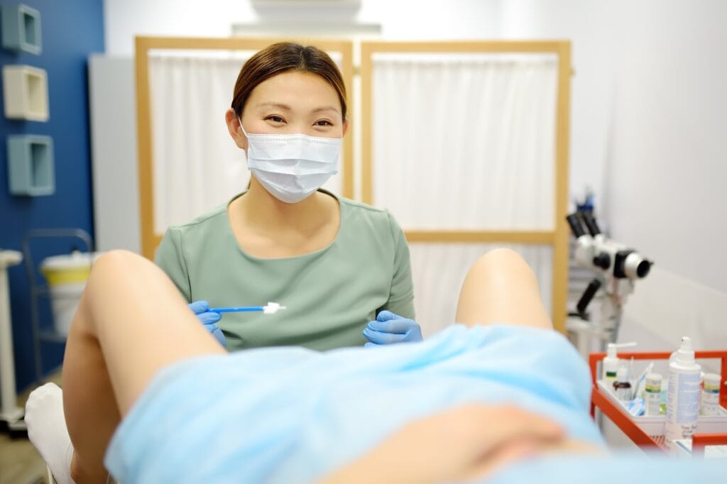 Gynecologist examines a patient laying on gynecological chair using medical vaginal speculum.